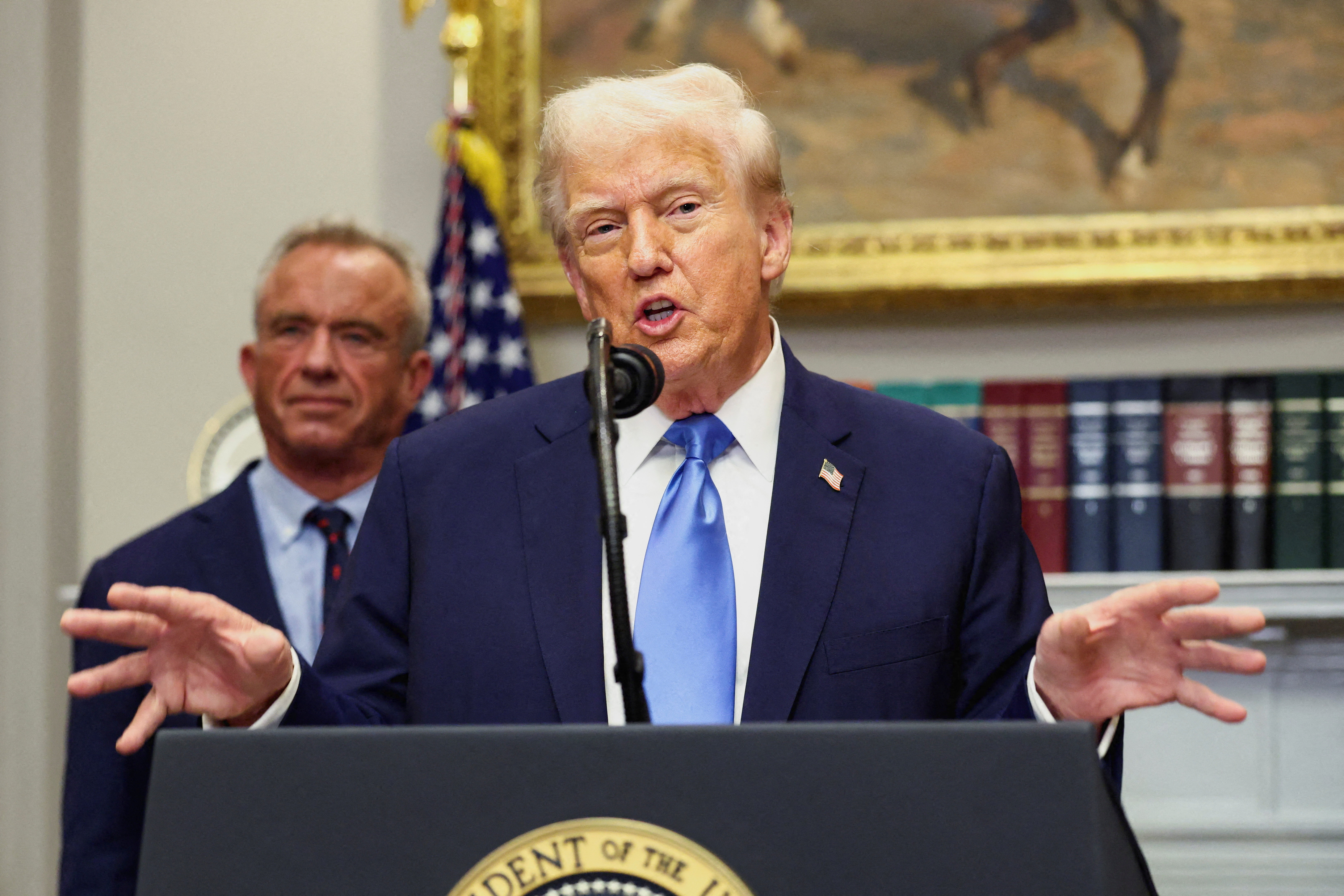 U.S. President Donald Trump speaks at a podium with Robert F. Kennedy Jr. standing behind him.