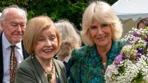 Getty Images Prunella Scales, with husband Timothy West in the background, alongside Queen Camilla, at a garden party in Rye last year.