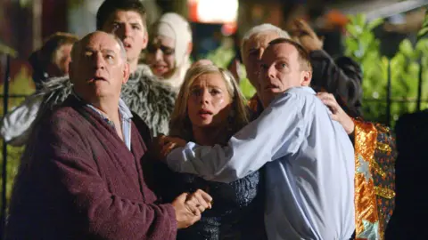 Tony Caunter (left as Roy Evans alongside other cast members of EastEnders looking shocked on Albert Square in 2002