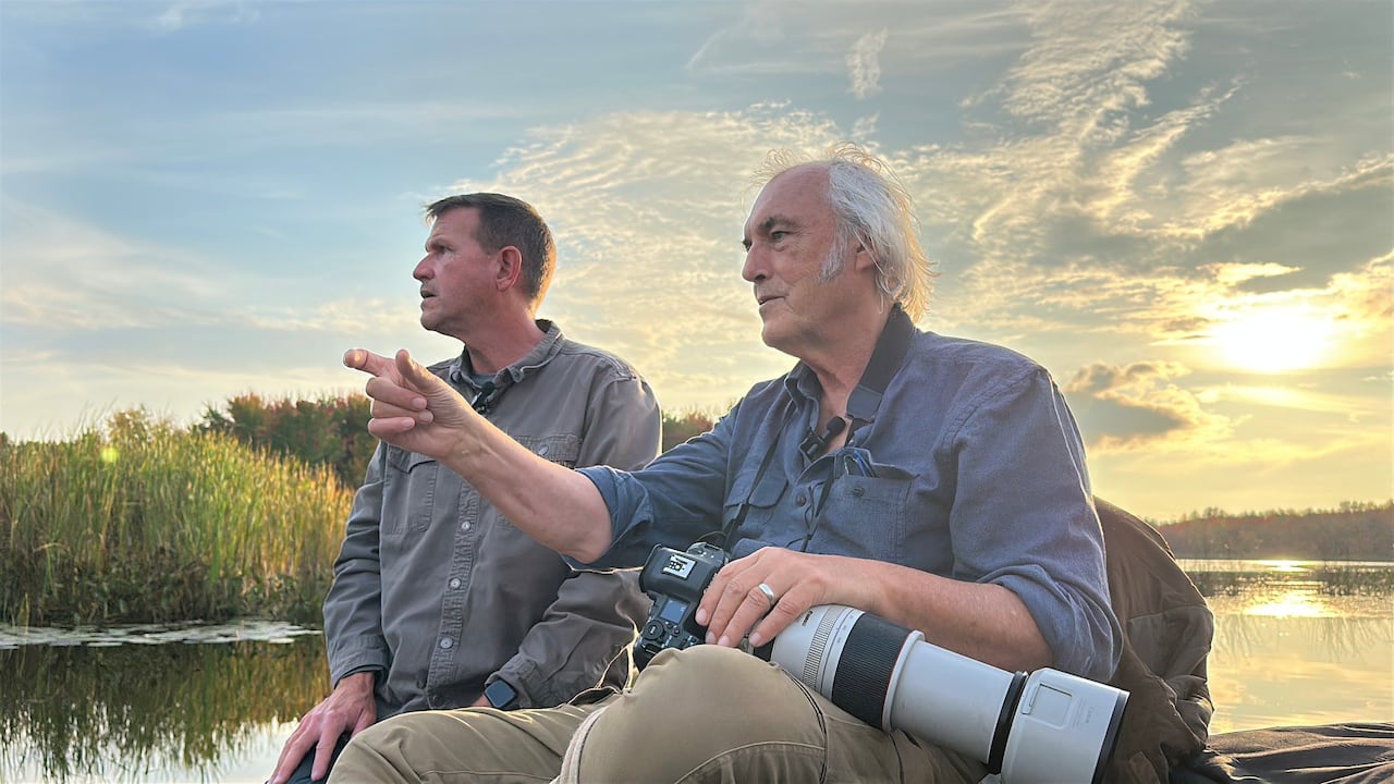 Two men on a boat at sunset, one holding a camera with large lens
