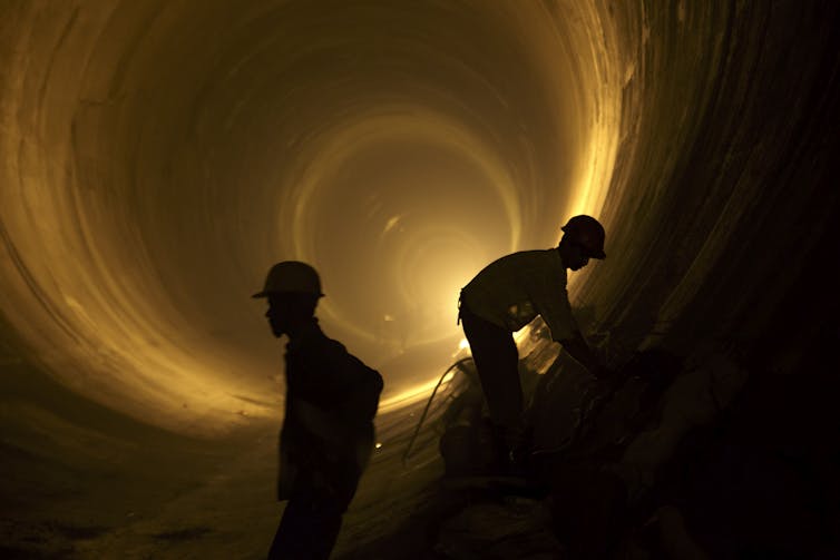 silhouette of two workers inside large tunnel, dimly lit.
