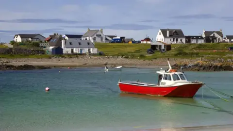 Getty Images A small fishing boat with a red hull is tied up in a shallow expanse of turquoise water. Land in the background is dotted with white houses. 