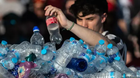 Getty Images A man adds an empty plastic bottle to a large pile of plastic bottles.