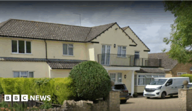 A two storey yellow building with a black iron balcony on the front of the property. A white van is parked outside.