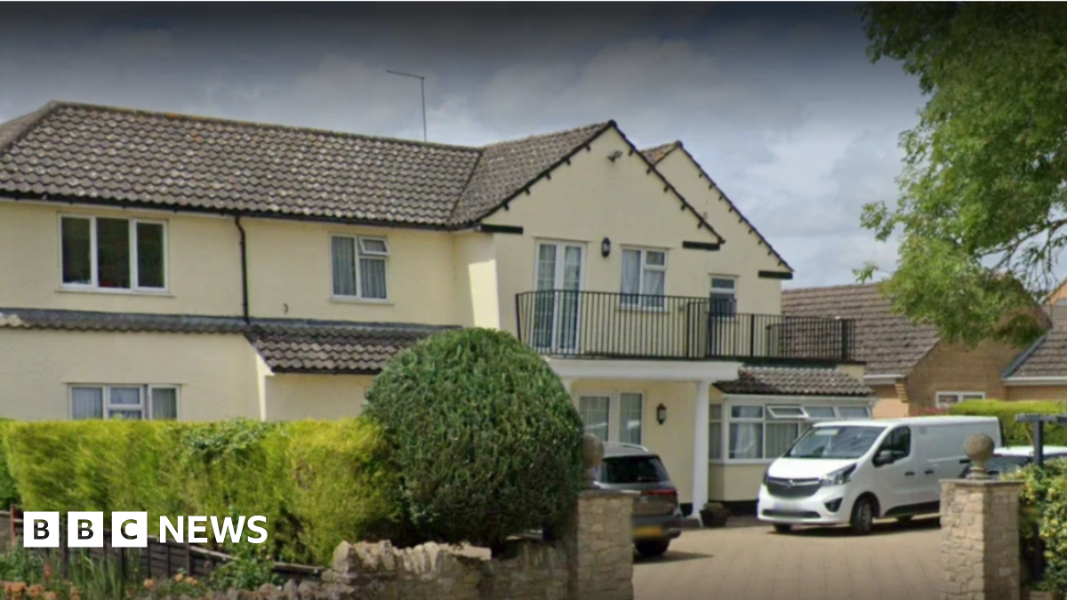 A two storey yellow building with a black iron balcony on the front of the property. A white van is parked outside.