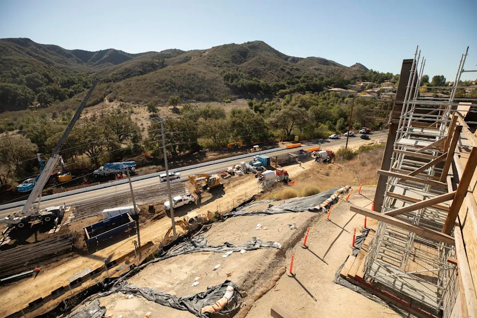 A tall crane rises above Agoura Road and the Stage 2 construction on the south side of the wildlife crossing.