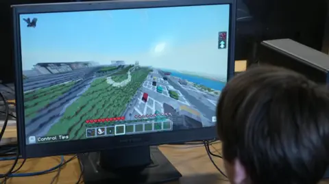 BBC A pupil sits in front of a computer screen showing Minecraft-style 3D graphics.