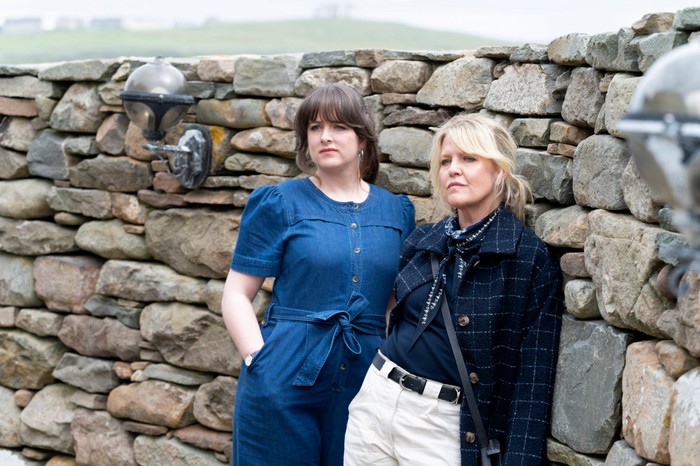 Alison O'Donnell as DI Tosh McIntosh and Ashley Jensen as DI Ruth Calder in Shetland, stood together, leaning against a brick wall