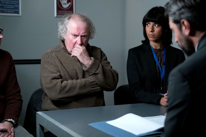 Nigel with a hand to his mouth as he sits next to a solicitor in EastEnders