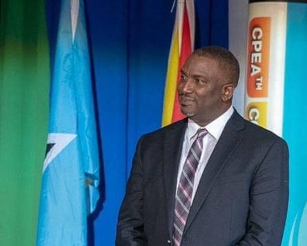 Donaldson Romeo: a formal photo in which he stands in front of flags, wearing a suit and tie. He has a close-shaven head and neat, short grey beard.