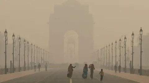 Reuters Women walk on a road near India Gate as the sky is enveloped with smog after Delhi's air quality worsened due to air pollution, in New Delhi, India, November 19, 2024. REUTERS/Anushree Fadnavis
