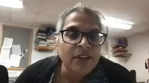 Orthopaedic Academy A video shot of Kuldeep Stohr giving a lecture to Orthopaedic Academy. She wears brown glasses and has hair tied back in a ponytail, wearing a black cardigan