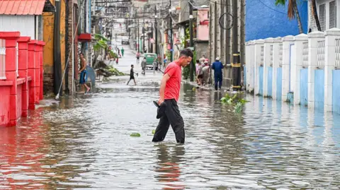 AFP via Getty Images A man walks through a flooded street in a neighbourhood affected by Hurricane Melissa in Santiago de Cuba.