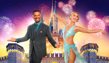 Dancing with the Stars cohosts Alfonso Ribeiro and Julianne Hough are seen in front of an image of a Disney park castle, with fireworks in the background; several fireworks on the right, behind Hough, are shaped like Mickey Mouse.