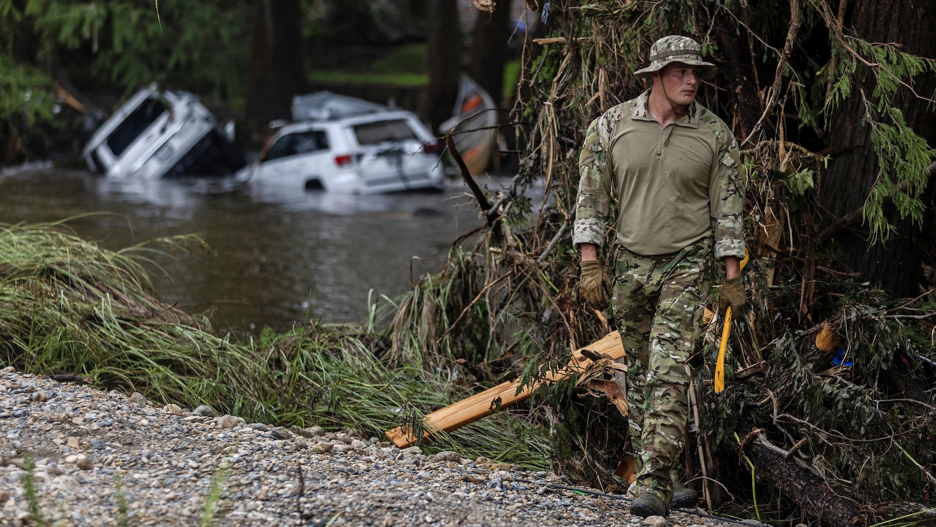 A search and rescue workers looks through debris along the Guadalupe River with half-sunk cars visible in the background
