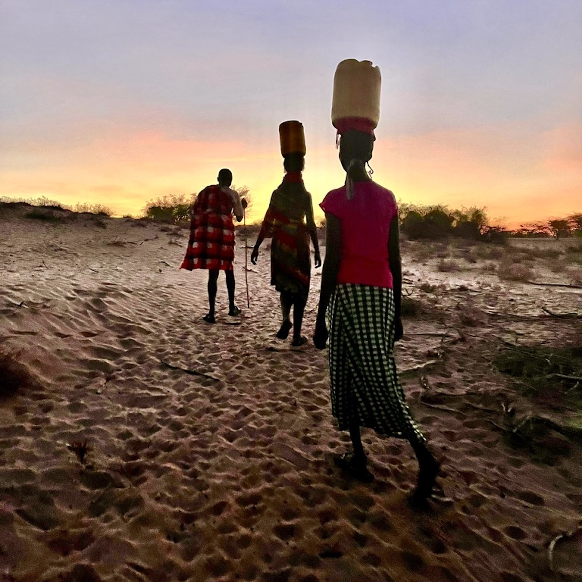 Three Kenyans walk with carrying supplies at sunset