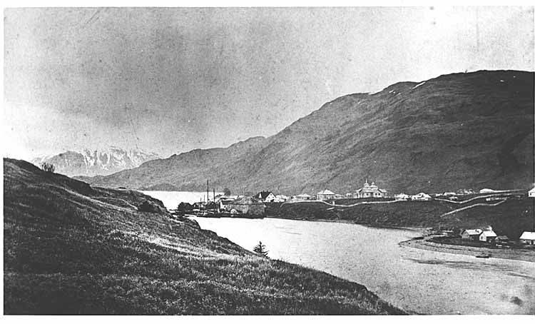 A black and white photo of a town on the edge of a river in a valley
