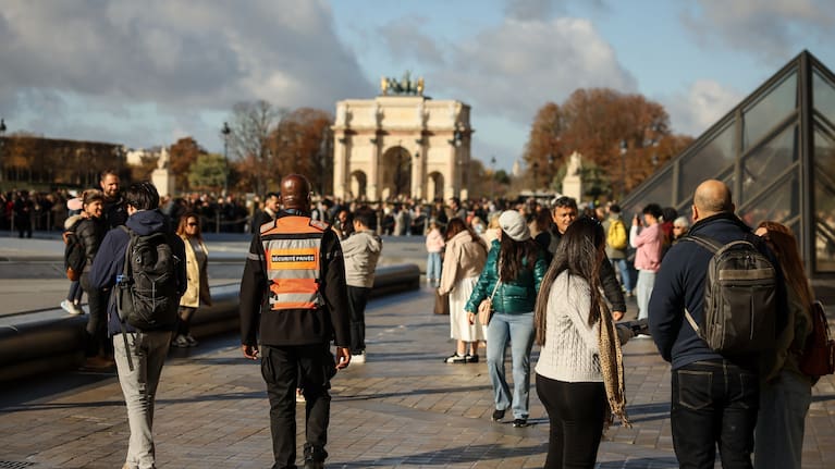 A member of a private security company, centre, and visitors walk in the courtyard of the Louvre museum.