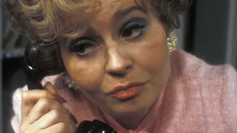 BBC Images Prunella Scales in a pink top on the phone as Sybil in Fawlty Towers