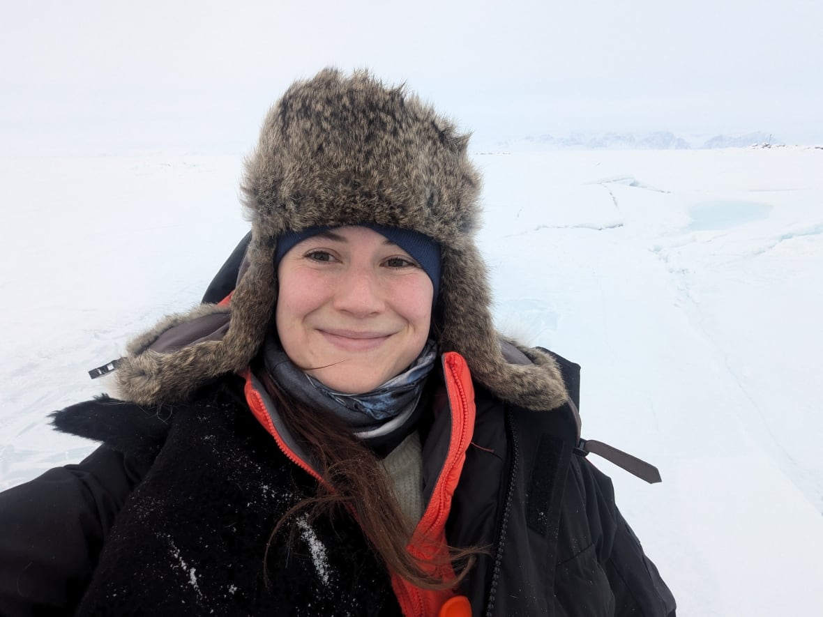 woman in parka and trapper hat stands on the sea ice.