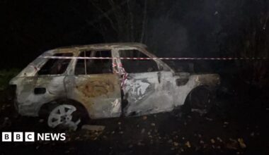 A burnt out white Range Rover in the dark with red and white tape around it