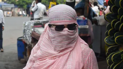 NurPhoto via Getty Images A woman covers her face while walking on the street during the heatwave in Kolkata, India, on April 20, 2025.