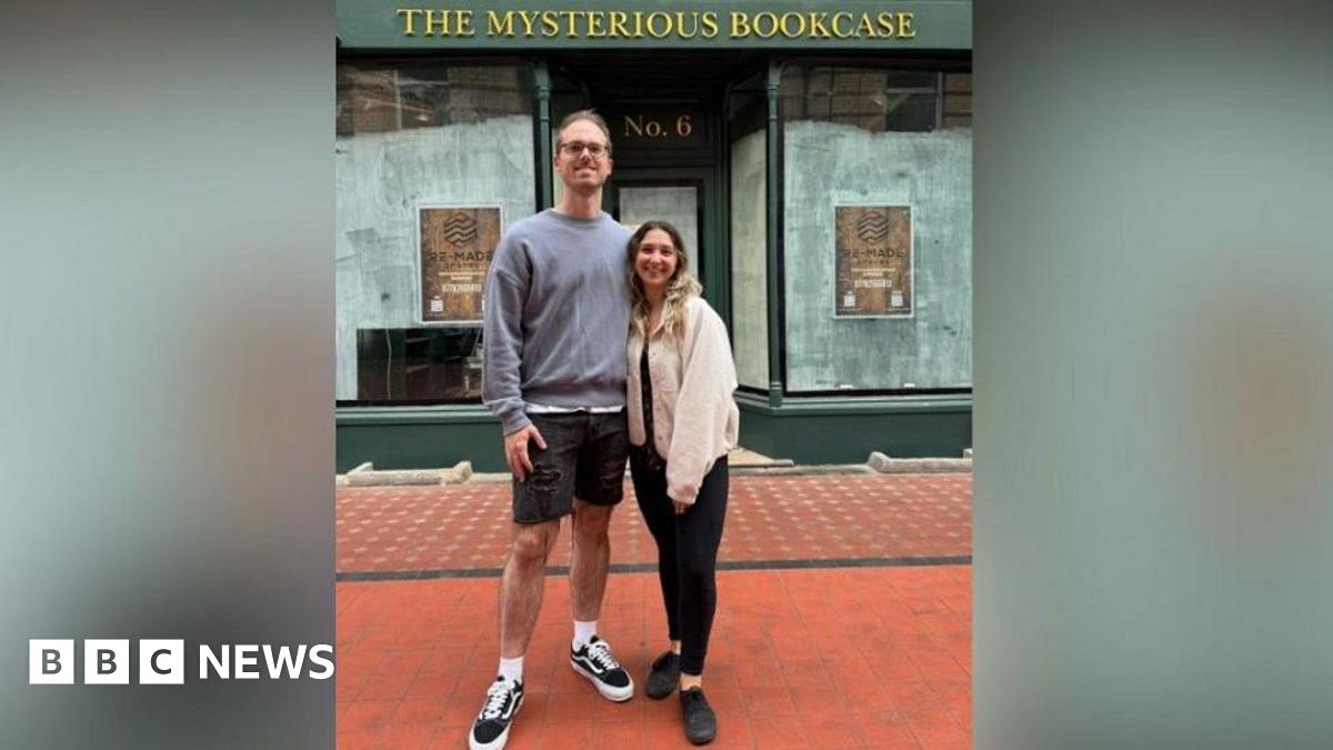 Ally Fir (R) and Matt Rawlings (L) pictured outside their shop before it opened. The windows are empty and there is a sign saying "The Mysterious Bookcase".