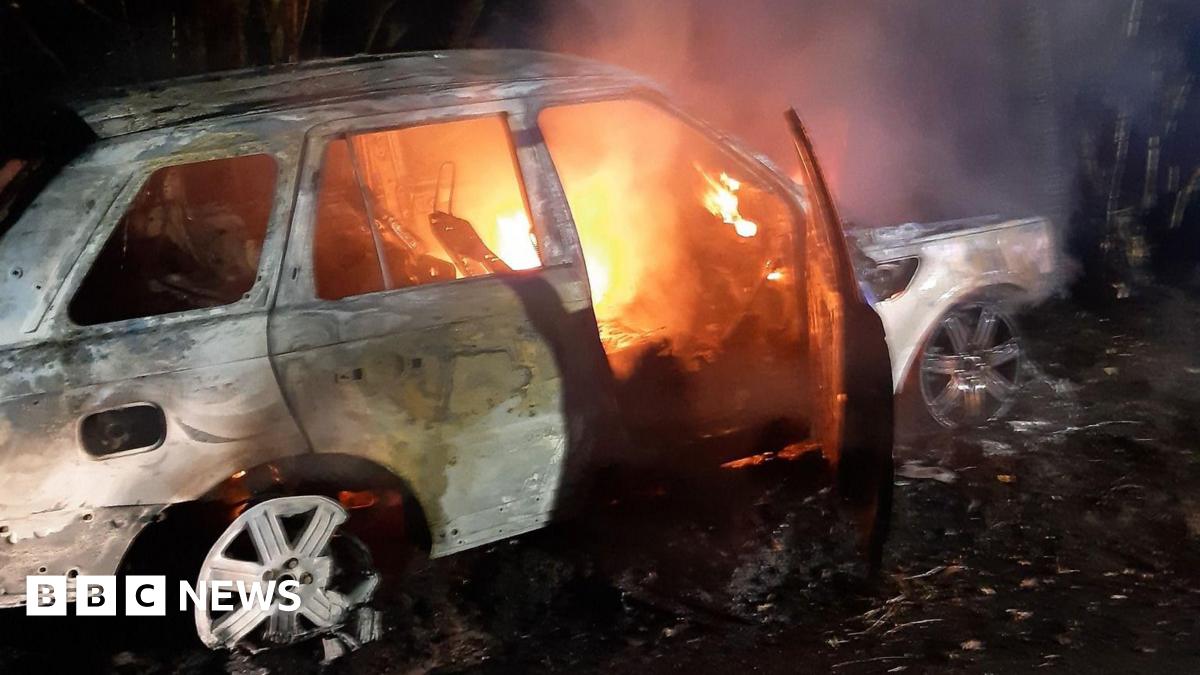 A white car with white wheel trims is engulfed in flames.