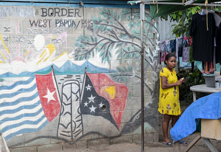Woman stands beside wall with flags mural
