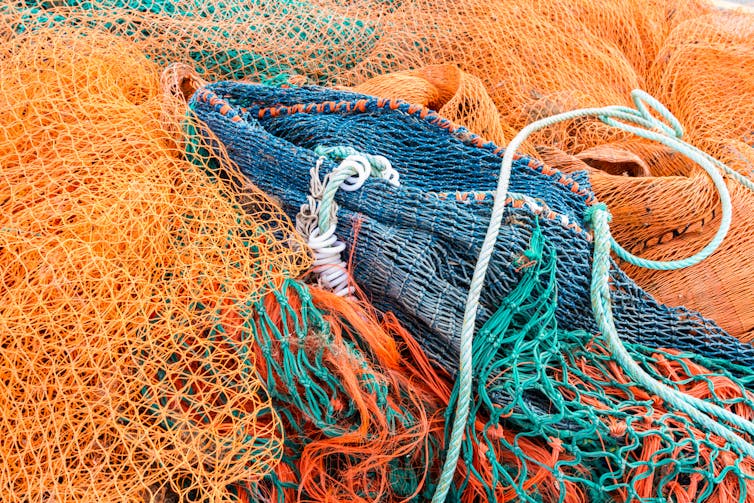 Orange and green colourful fishing nets lying in pile on land
