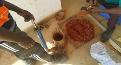 Two people standing around a pile of soil and plastic, mixing it
