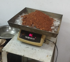 An old fashioned scale with a pile of red soil mixed with cut up transparent plastic bottles