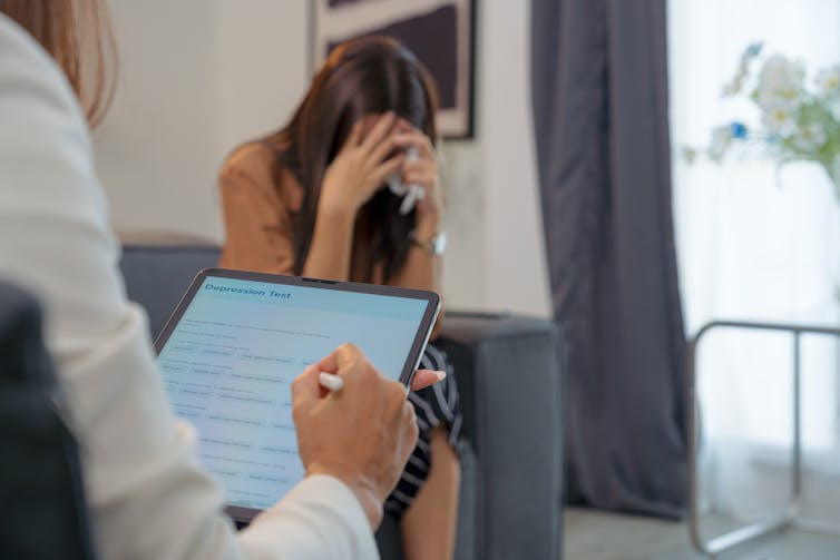 A woman hides her face as a therapist conducts a depression screening