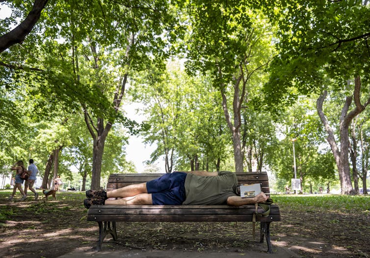 a man lies on his side on a park bench reading a book