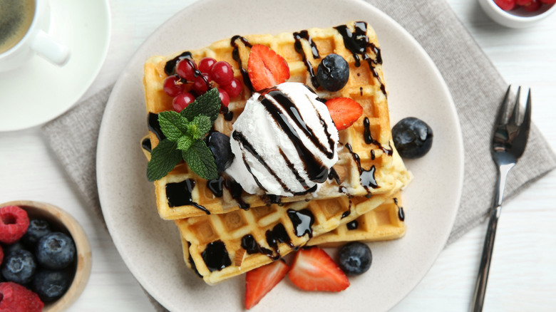 Waffles topped with ice cream, chocolate sauce, and berries