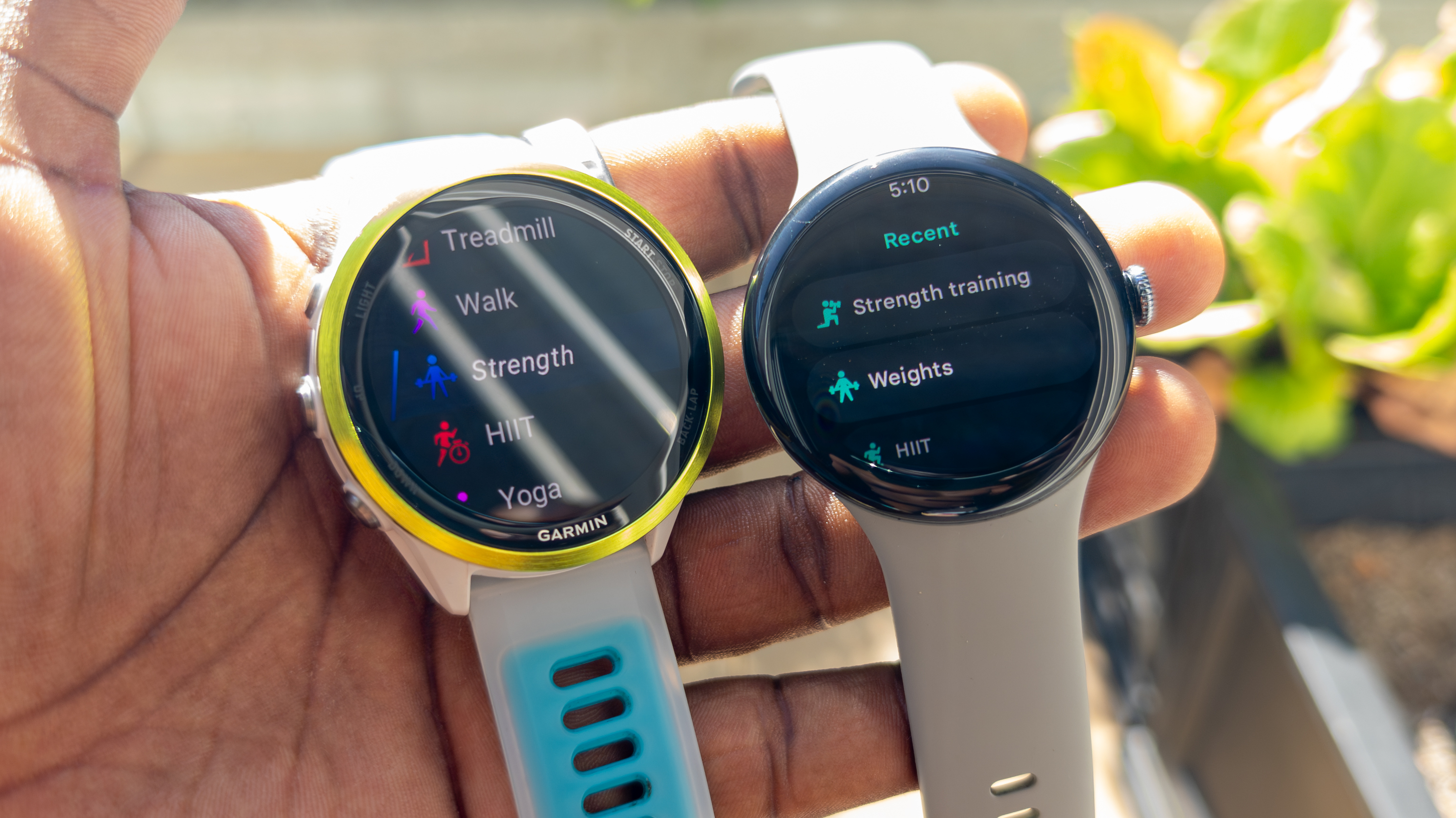 Holding the Garmin Forerunner 570 and Google Pixel Watch 3, both displaying workout modes