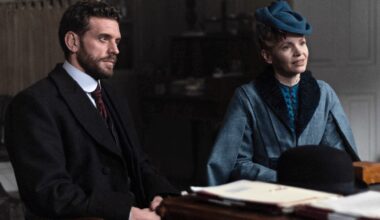 Color image of a scene from Miss Scarlet Season 6 on MASTERPIECE on PBS. Actor Tom Durant-Pritchard as DI Alexander Black is seated next to Kate Phillips as Eliza Scarlet behind a desk.
