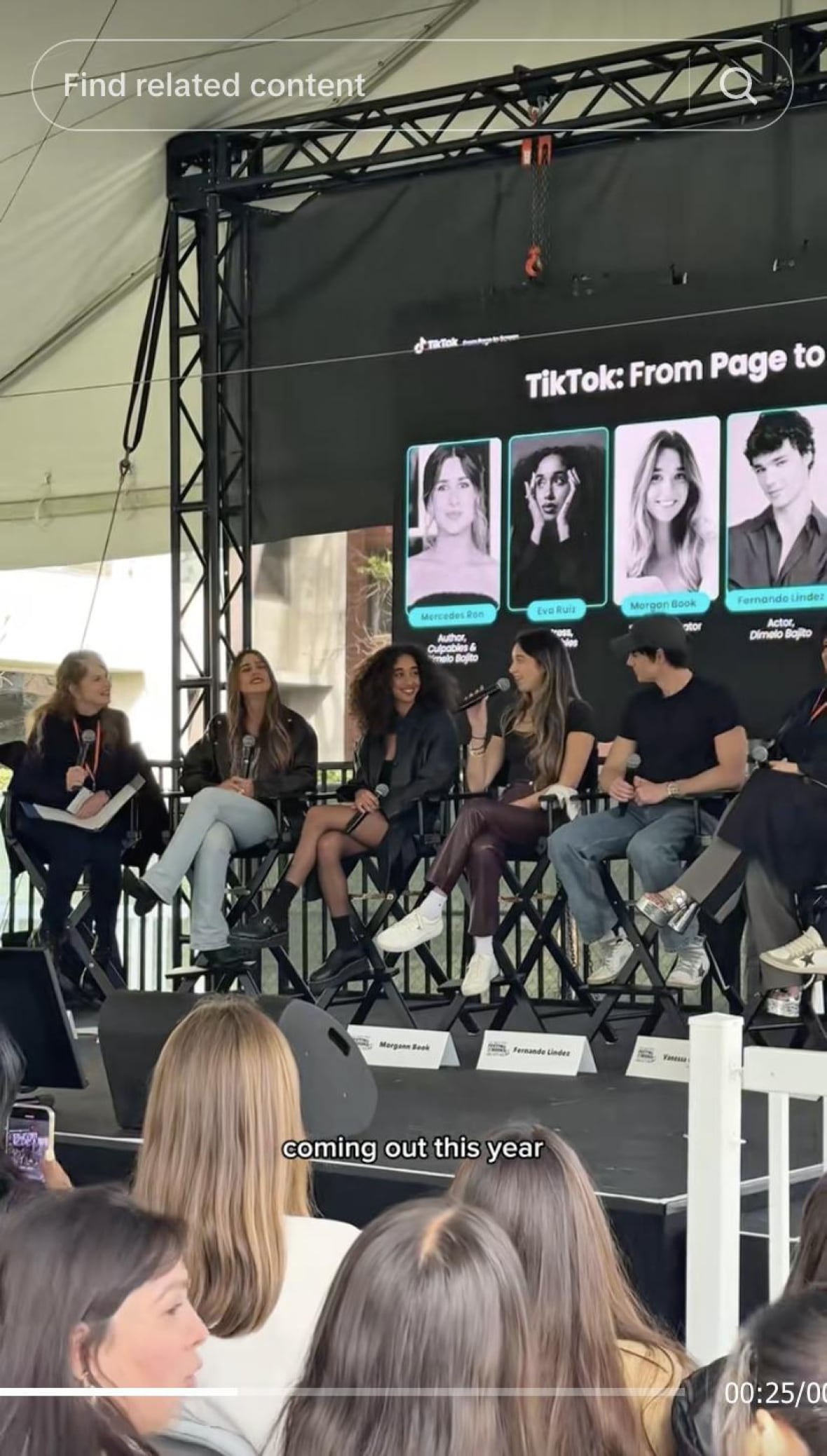 A panel of 5 people sit on stage with microphones.