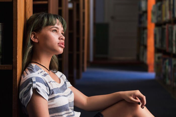 Young woman sitting against a bookshelf looking thoughtful, illustrating patients brushing off terrifying symptoms ignored by doctors.