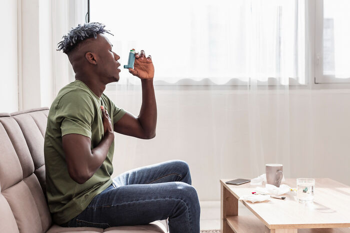 Man using an inhaler for breathing symptoms at home, highlighting patients brushing off terrifying symptoms as normal.
