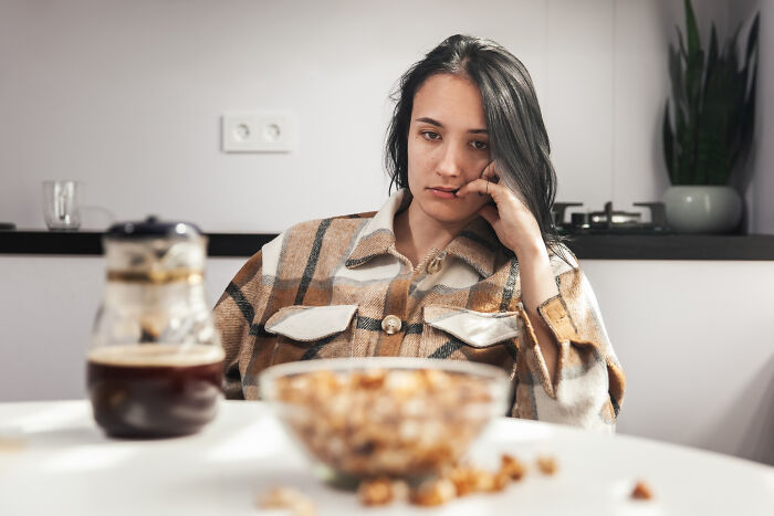 Young woman sitting at kitchen table looking worried and brushing off terrifying symptoms as normal health concerns.