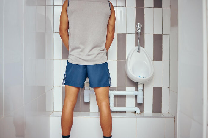 Man standing at a urinal in a public restroom, representing patients brushing off terrifying symptoms as normal.