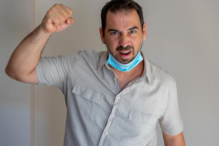Man with lowered face mask making a fist gesture, expressing frustration about patients brushing off terrifying symptoms.