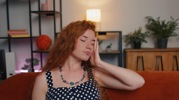 Young woman with red hair sitting on a couch, appearing distressed and holding her head, illustrating patients brushing off symptoms.