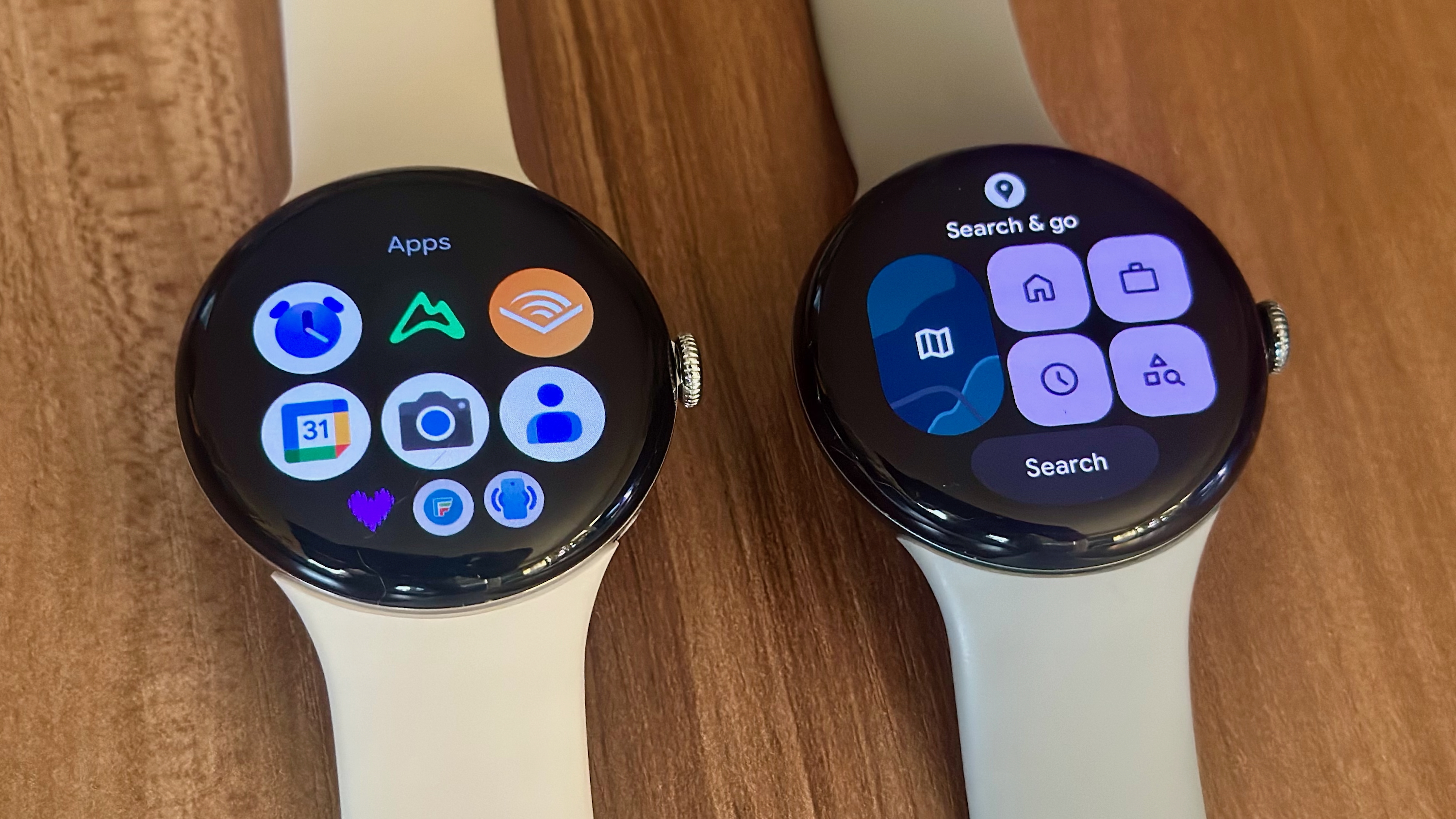 The Google Pixel Watch 4 (left) showing the app drawer on display, next to the Pixel Watch 3 showing the Google Maps Tile
