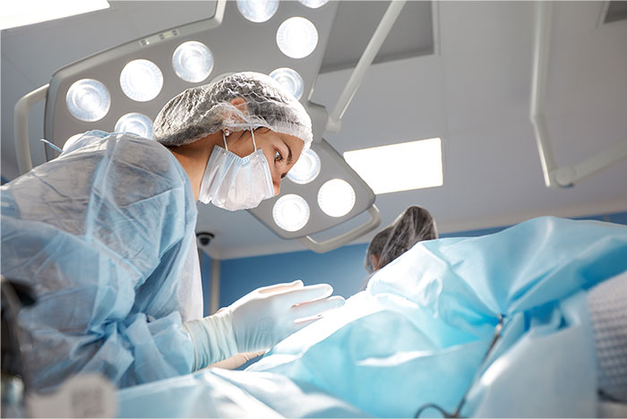 Surgeon in sterile gear performing surgery under bright operating room lights during a medical procedure.