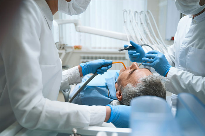Patient undergoing surgery with medical team using tools and wearing protective masks and gloves in operating room
