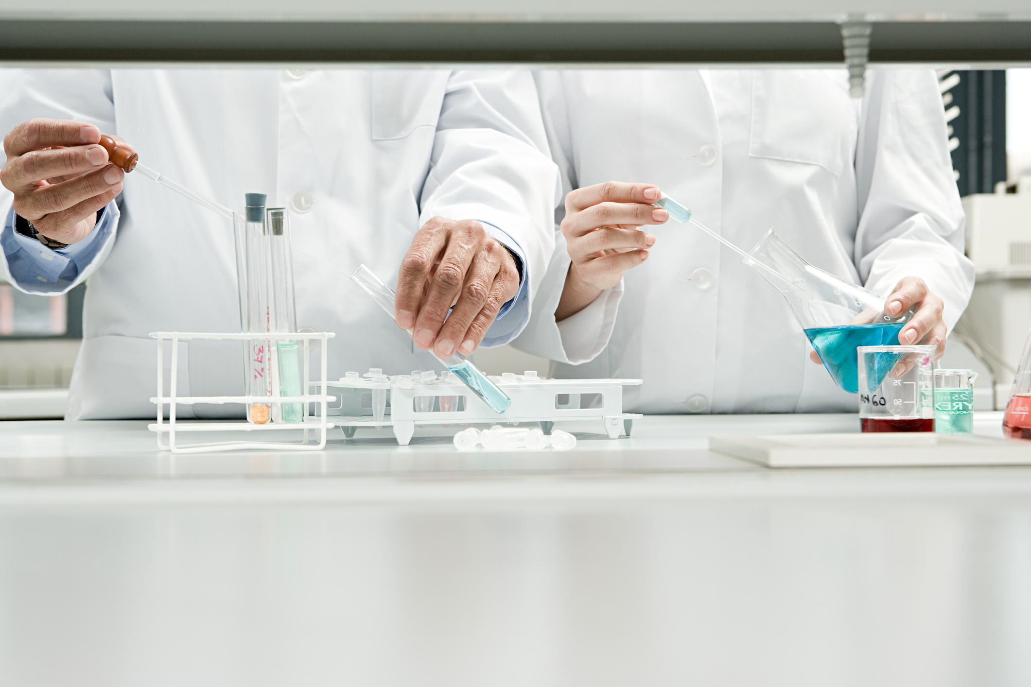 people wearing lab coats hold scientific instruments like beakers and test tubes while standing at a table