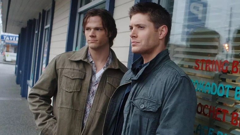 Sam Winchester (Jared Padalecki) and Dean Winchester (Jensen Ackles) stand in front of a storefront window on Supernatural