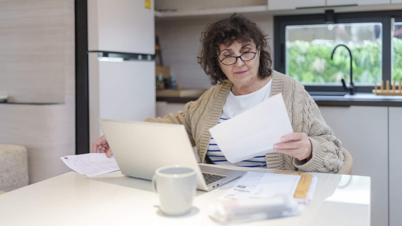 A woman sitting at a table where she has her laptop open as she looks at bills.